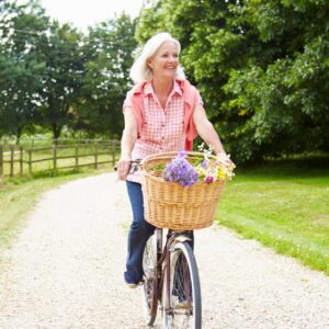 middle-aged woman riding a bike on a gravel path with flowers in the basket