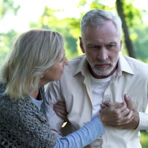 Umbilical Cord Stem Cells for Heart Failure An older man clutching his chest in distress or pain while a concerned woman leans in to support him outdoors.